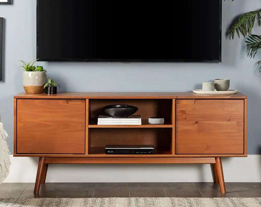 A sleek and modern living space showcasing a flat-screen TV mounted above a mid-century style wooden TV stand. The stand has closed compartments on both sides and open shelves in the middle, perfect for storing media devices and decorative items. The setup is enhanced with potted plants and minimalist decor.